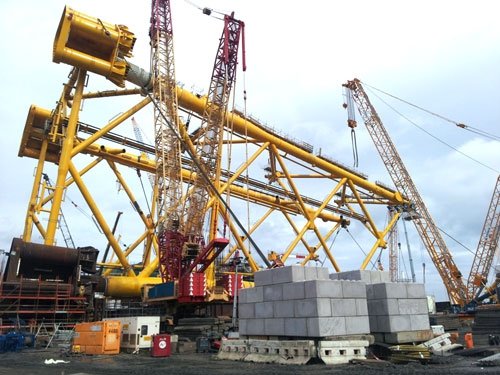 Stacked kentledge blocks ballasting a large yellow crawler crane on site