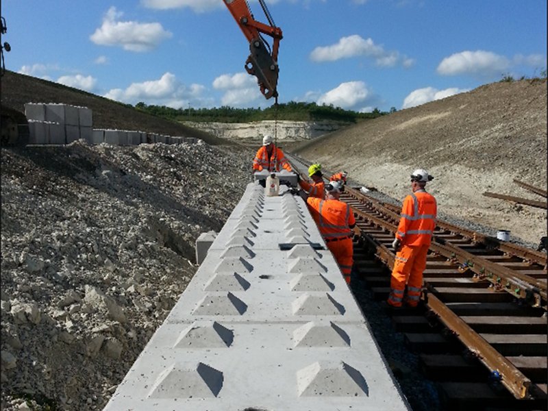 Rail workers laying track beside a new precast concrete safety wall