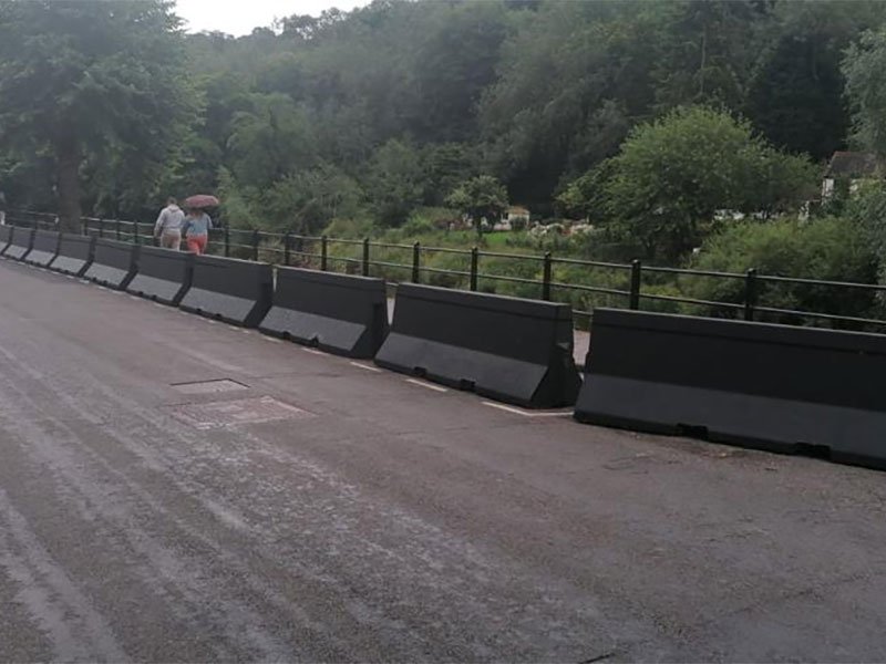 Black Jersey barriers lining a road with a pedestrian walking behind them