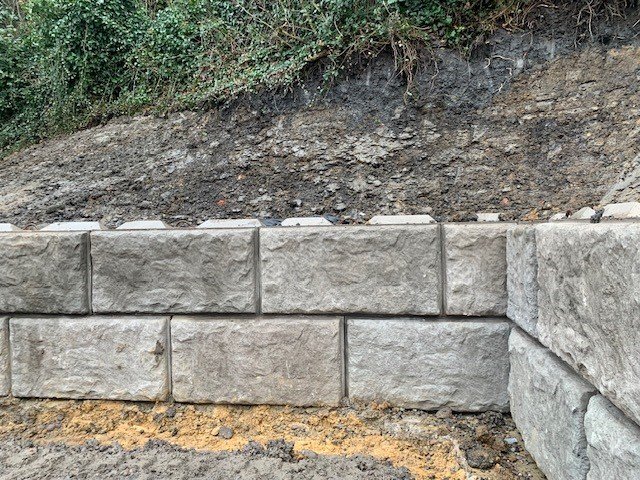 Rock-faced walling blocks forming a low retaining wall below a vegetated bank