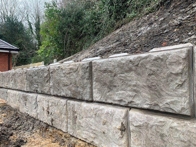 Two courses of rock-faced Vee-Rock blocks retaining a steep excavated earth bank