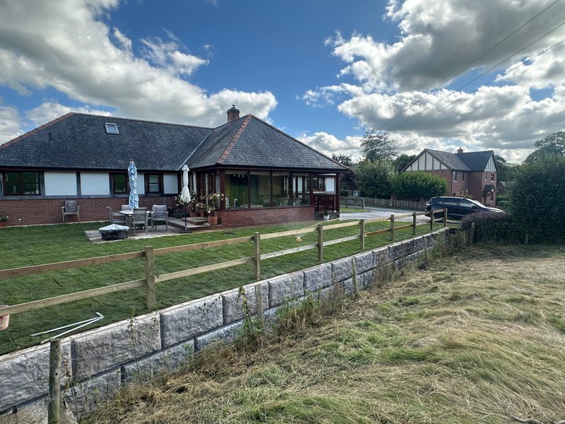 Rock-faced Vee-Rock retaining wall and timber fence along the lawn of a bungalow