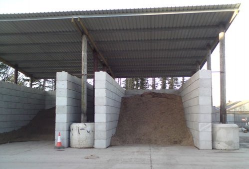 Covered compost storage bay with interlocking block dividing walls under a steel canopy