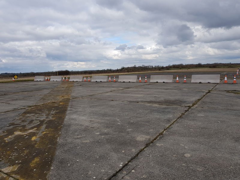 Line of Jersey barriers and cones stretching across an airfield apron