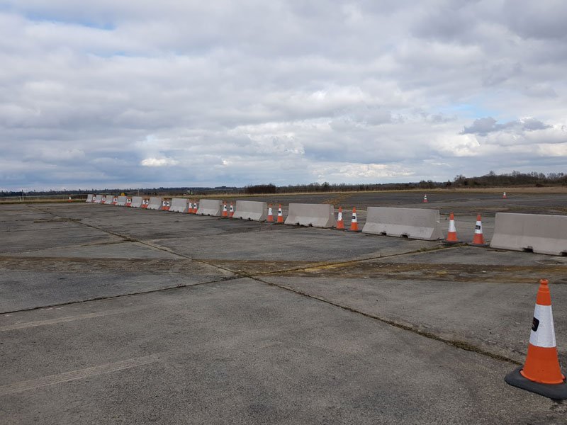 Line of concrete barriers and cones across an airfield apron