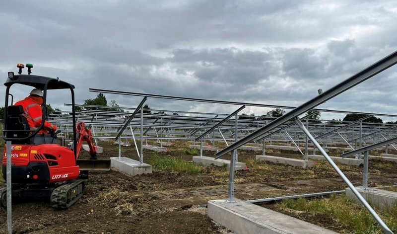 Mini excavator working among solar panel frames set on concrete ballast blocks