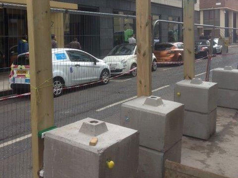 Ballast blocks anchoring timber hoarding posts along a street footway
