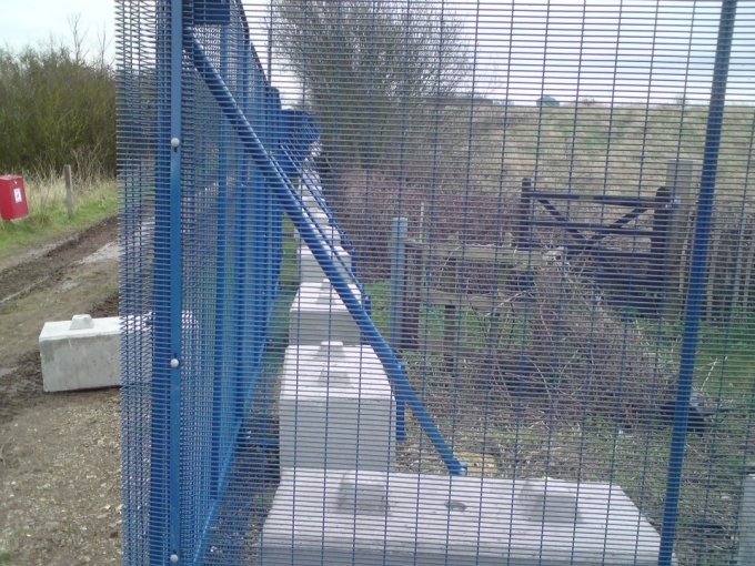 Concrete kentledge ballast block weighting the base of a blue mesh fence post