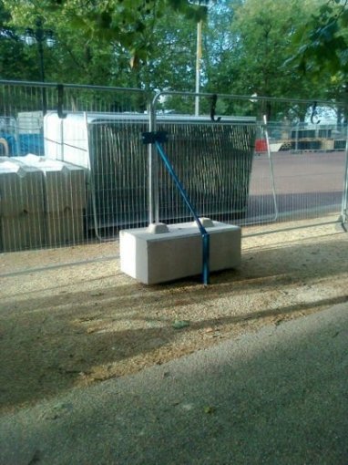 Concrete ballast block bracing a temporary mesh fence panel on a grass verge