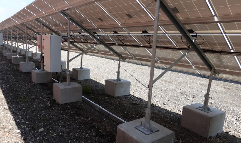 Concrete ballast blocks supporting the frame legs of a ground-mounted solar array
