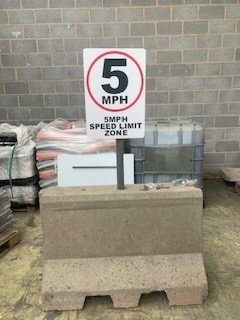 Concrete ballast barrier block anchoring a 5mph speed limit sign against a wall