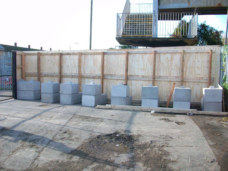 Kentledge blocks ballasting a run of timber hoarding across a construction site