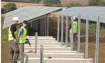 Workers fixing solar mounting frames onto a row of concrete ballast blocks
