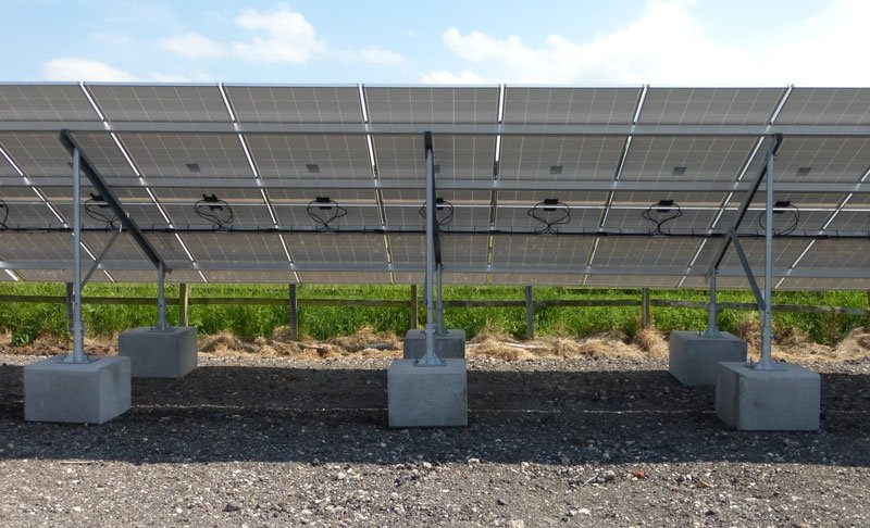 Concrete ballast blocks anchoring solar panel frames on a gravel bed