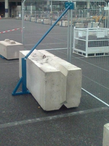 V-shaped kentledge ballast block weighting a temporary fence brace on a tarmac yard