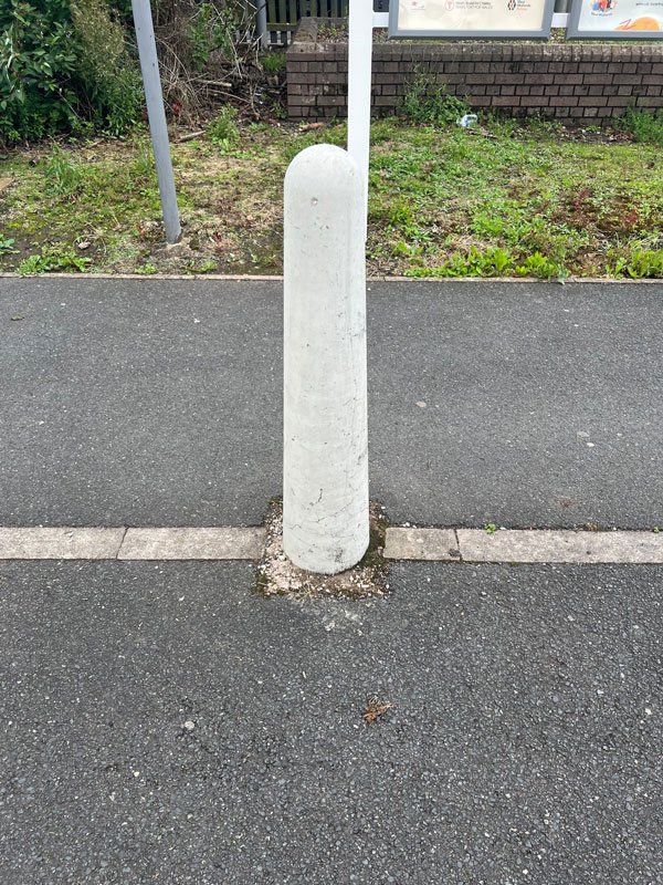 White precast concrete bollard set in a pavement beside a kerbed road