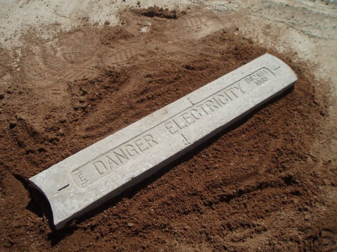 Cable protection cover marked Danger Electricity laid in an open soil trench