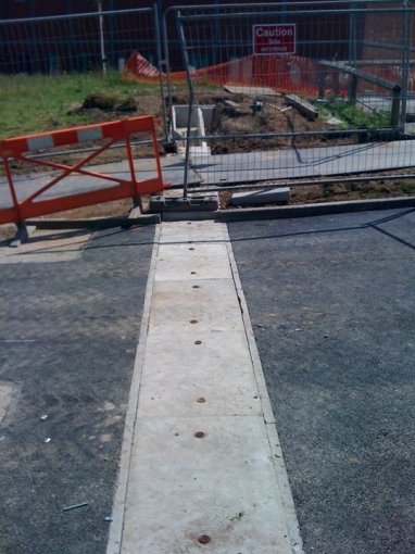 Precast channel with cover slabs running across a fenced construction site