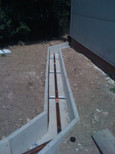 Precast channel run beside a building carrying pipework in an open trench