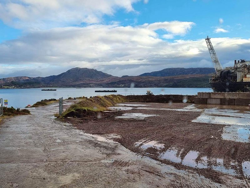 Coastal decommissioning yard beside a sea loch with a crane and hardstanding