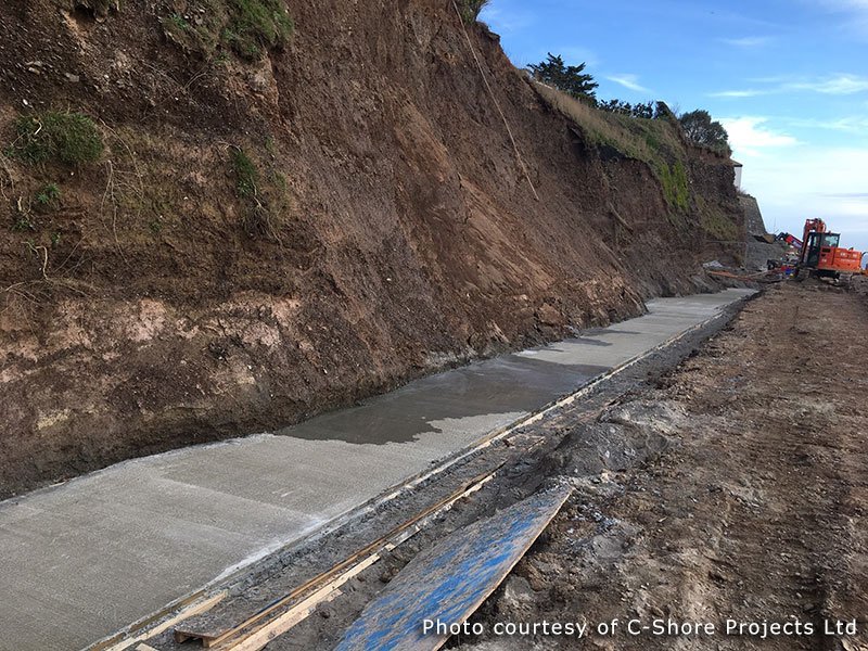Concrete foundation strip poured along the toe of an eroding coastal cliff