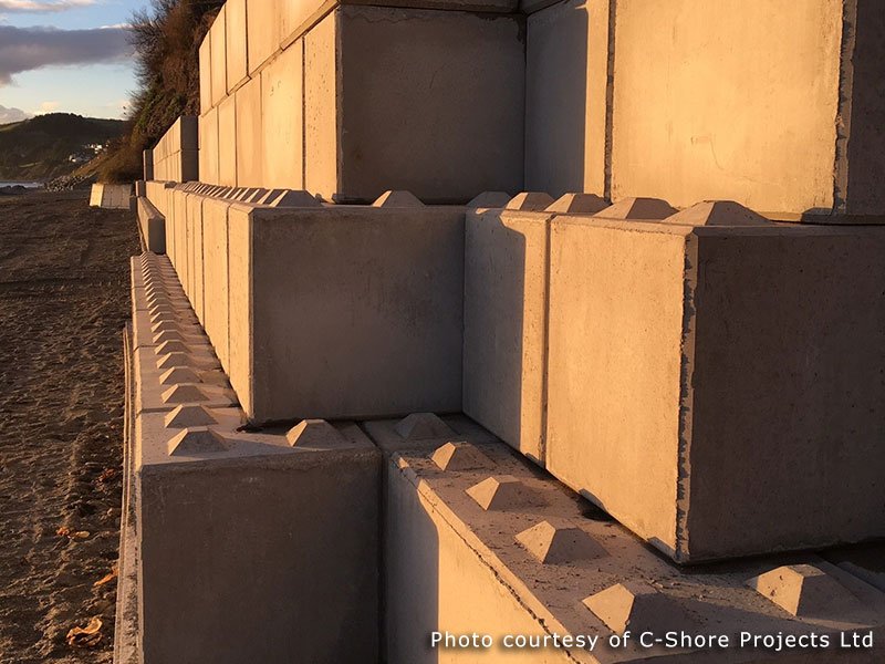 Interlocking blocks stacked into a coastal retaining wall lit by low sun