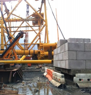 Stacked counterweight blocks anchoring stand jacks beside yellow crane rigging