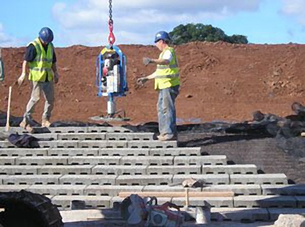 Workers using a lifting clamp to place dam spillway blocks on an embankment