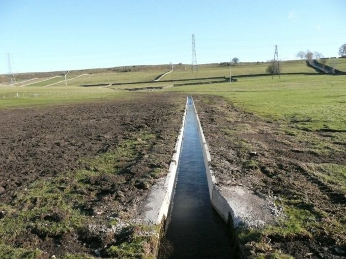 Precast concrete drainage channel running downhill across open farmland