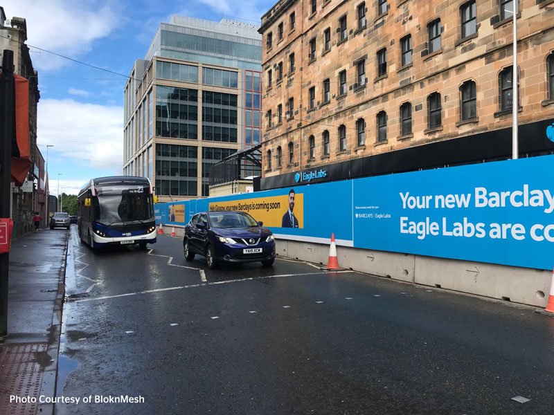 Hoarding panels lining a city centre street with a bus and traffic cones