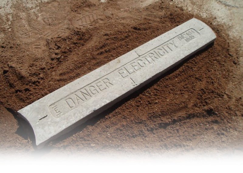 Cable protection cover marked Danger Electricity resting on freshly dug soil