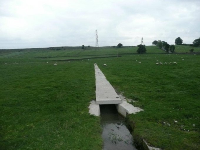 Precast concrete field drain channel crossing pasture into an open ditch