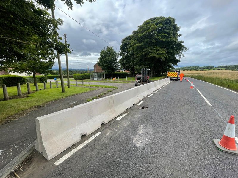 Jersey barriers lining a rural road closure with a traffic cone alongside