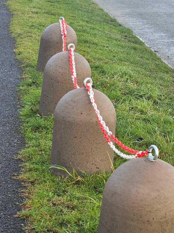 Dome-topped concrete bollards linked by red and white chain on a grass bank
