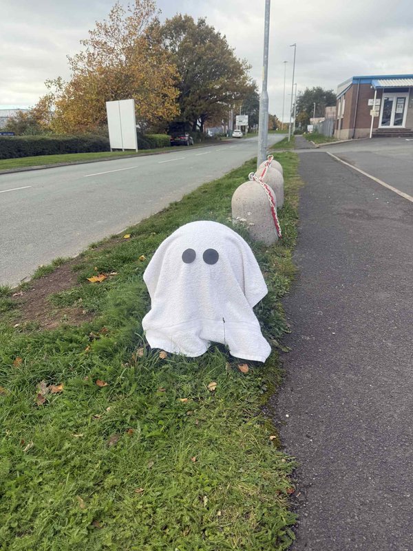 Concrete bollard dressed as a ghost with a white sheet on a verge