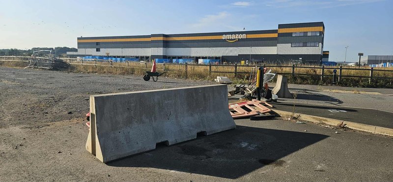 Jersey barrier standing on cleared ground outside a large distribution warehouse
