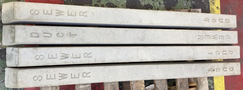 Concrete marker posts cast with sewer and duct lettering stacked on a pallet