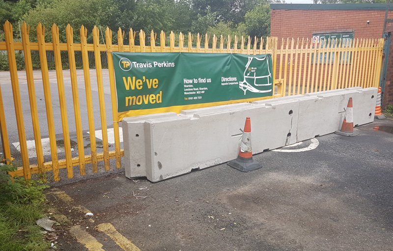 Concrete barriers lining a yellow palisade fence beside a builders merchant banner