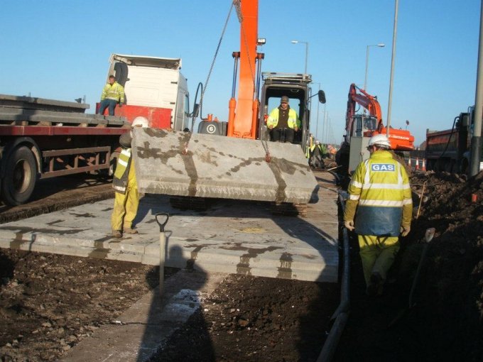 Workers laying precast protection slabs over a service trench beside a lorry