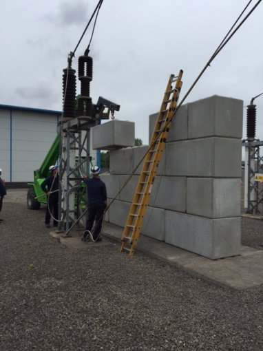 Precast blocks stacked as a blast wall beside substation switchgear with workers nearby