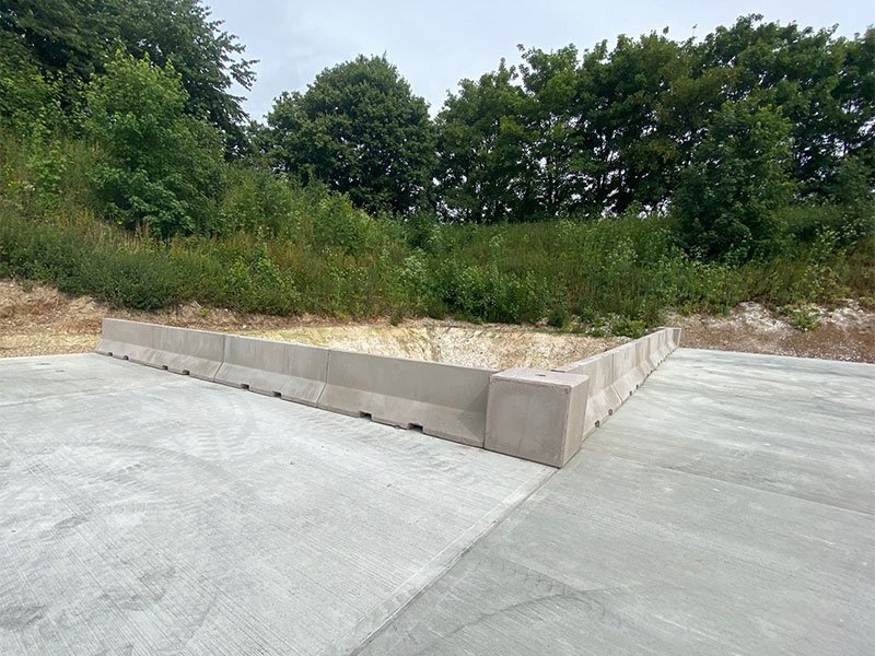 Low precast concrete barrier edging a newly poured concrete yard slab beside scrub