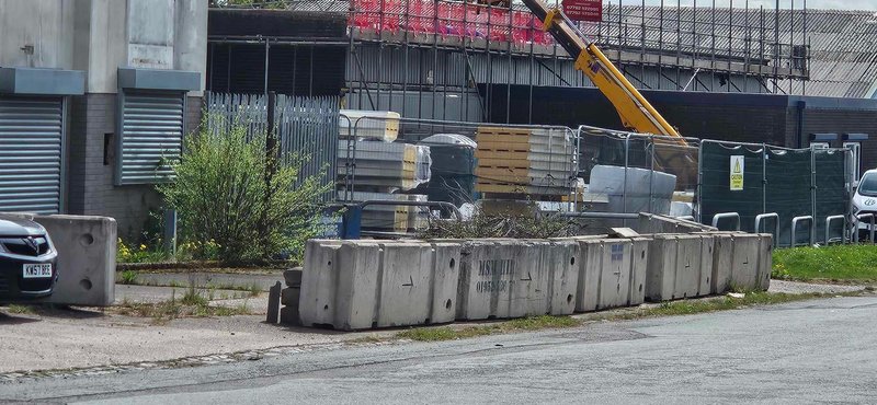 Line of temporary vertical concrete barriers securing a fenced roadside compound