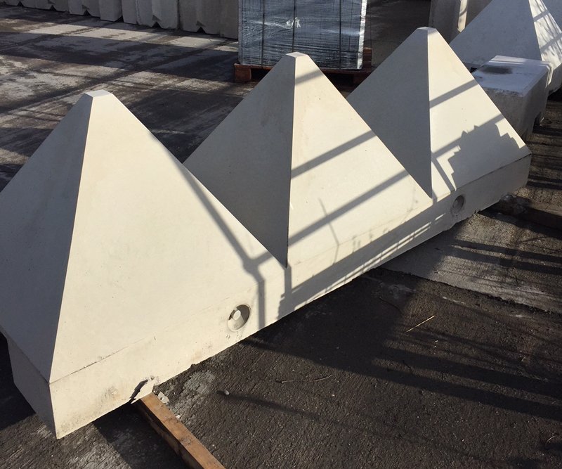 Tank trap pyramid barrier unit set on tarmac beside stacked precast products