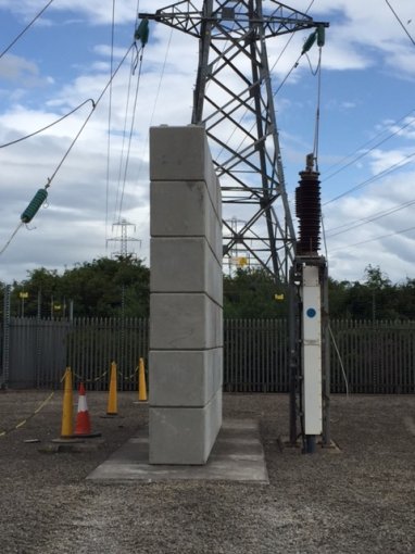 Precast concrete blast protection piers standing beneath pylon insulators at a substation