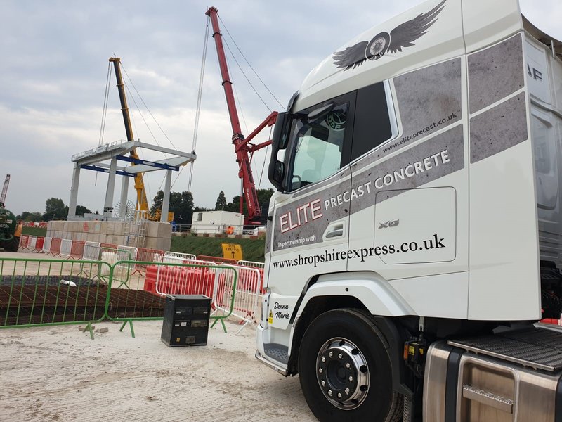Lorry crane lifting blocks into place on a fenced construction site