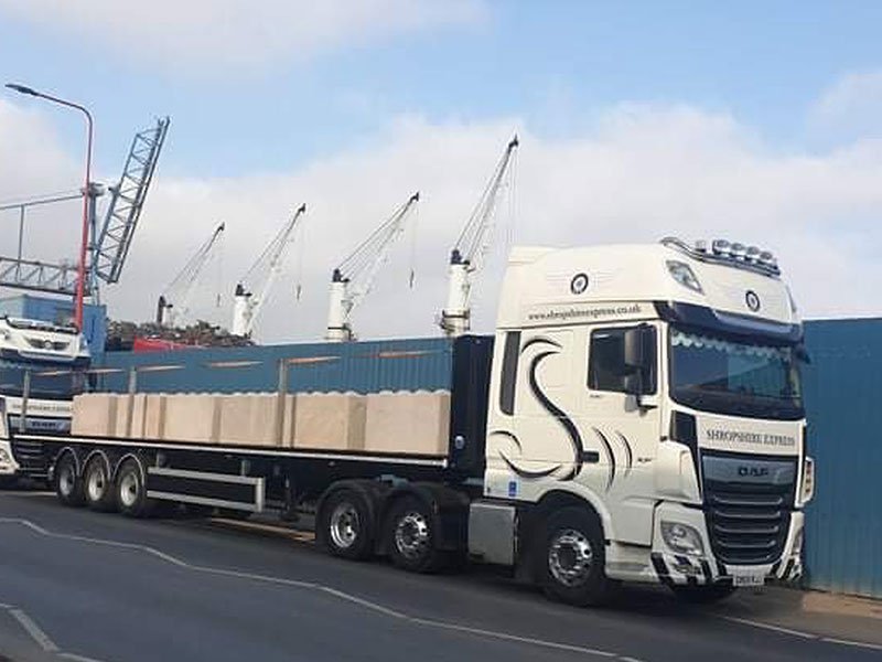 Flatbed lorry loaded with Legato blocks parked at a port beside dockside cranes