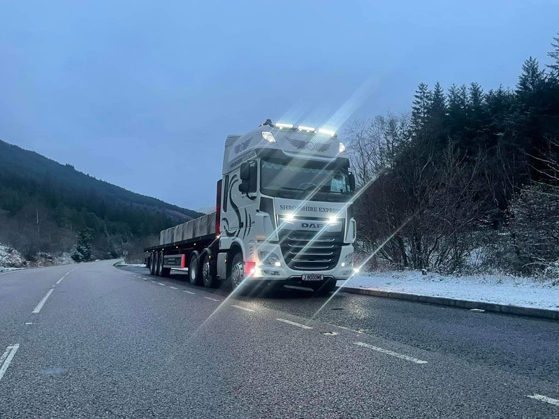 Articulated delivery lorry on a snow-lined highland road at dusk