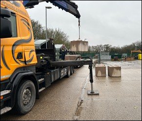 Lorry-mounted crane offloading concrete blocks from a flatbed trailer