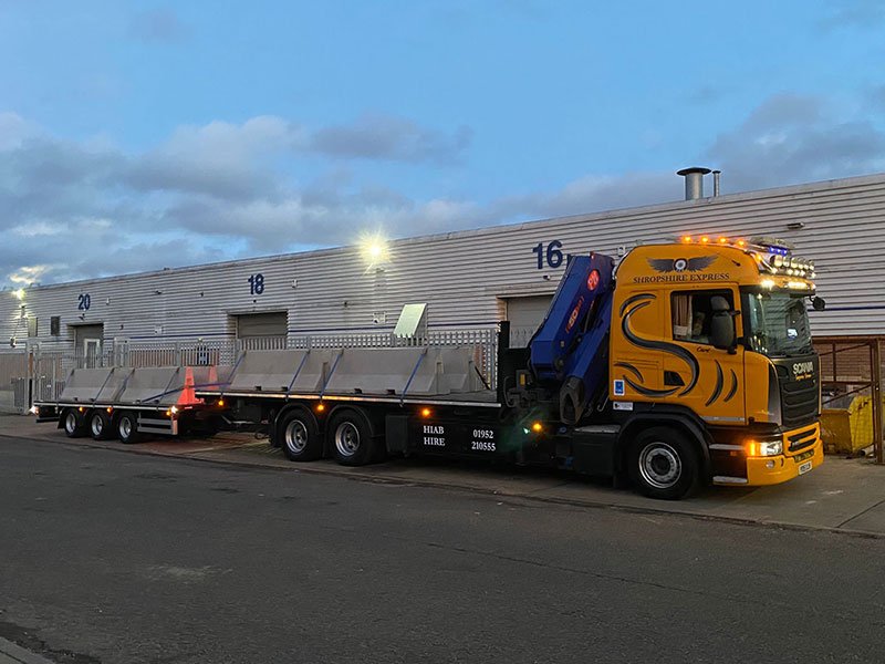 Articulated lorry and drag trailer with crane parked at a warehouse loading yard