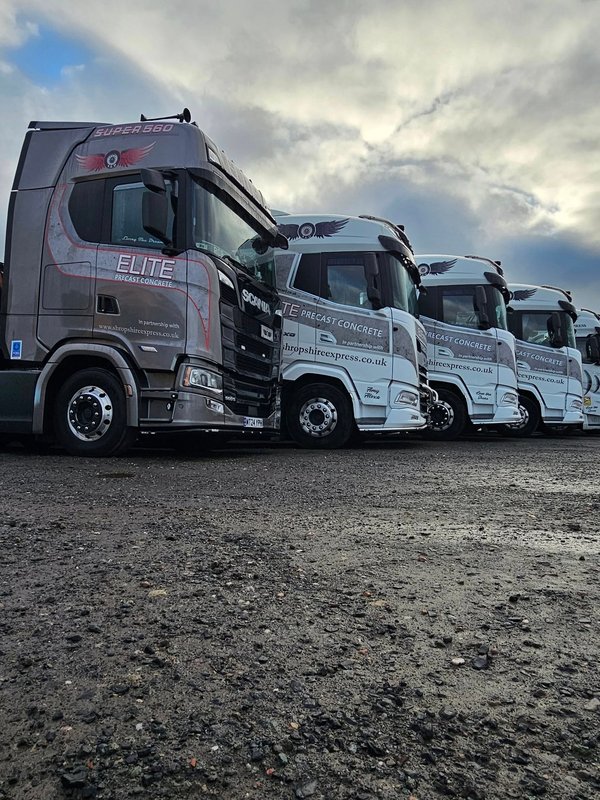Fleet of crane equipped delivery lorries parked in a yard at dusk